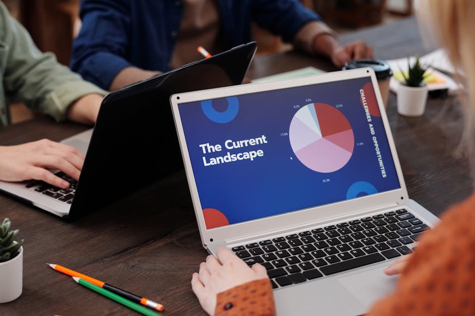 A team collaborates during a business meeting using laptops, analyzing data graphs.